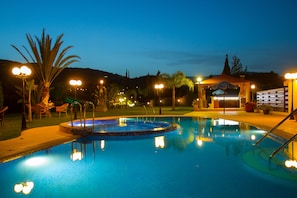 A swimming pool with a hot tub, surrounded by palm trees and outdoor seating. - Villa Anasia (Paralimni)