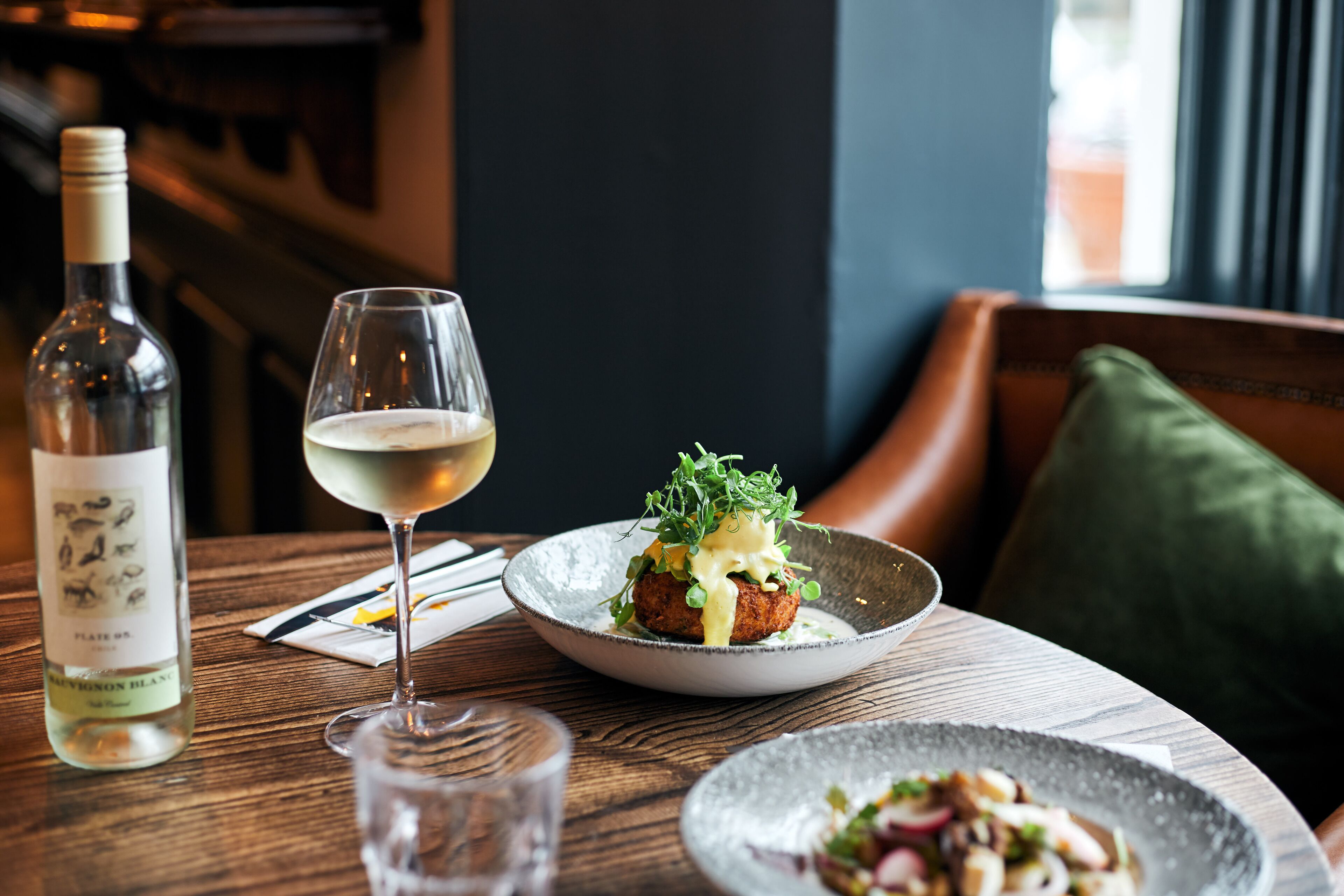 Una mesa de comedor con una botella de vino, una copa de vino blanco y un plato de comida.