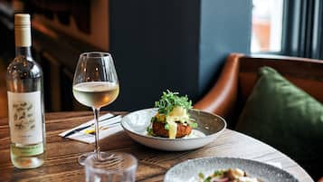 Una mesa de comedor con una botella de vino, una copa de vino blanco y un plato de comida.