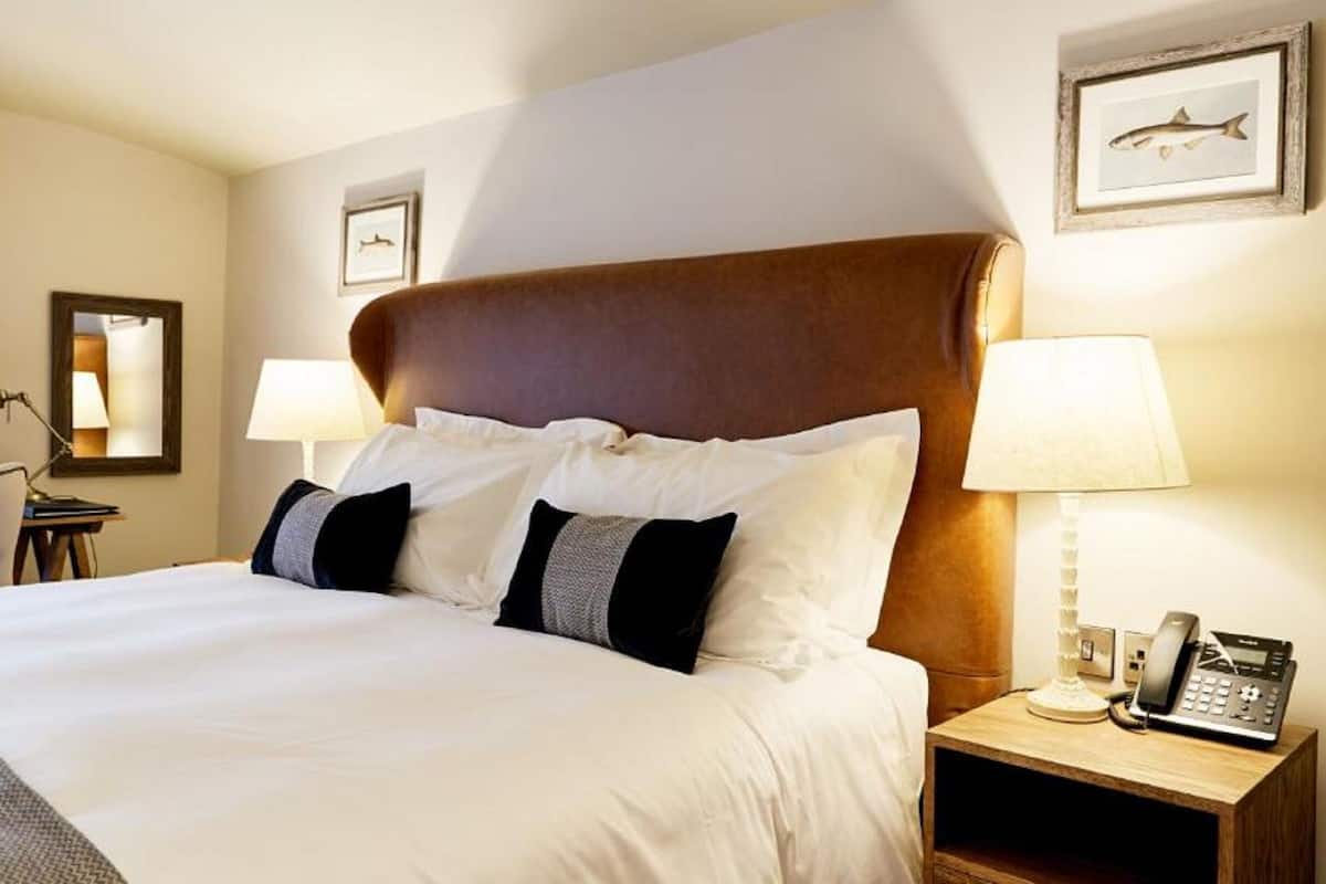 A hotel room with a large bed, two bedside lamps, a phone on the nightstand, and framed pictures on the walls.