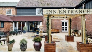 An outdoor seating area with a wooden archway labeled "INN ENTRANCE" leading to a brick building. There are potted plants and outdoor furniture. - The Wellington Arms (Hook)