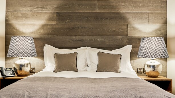A bedroom with a wooden headboard, two bedside lamps, a telephone, and a patterned bedspread. - The Wellington Arms (Hook)
