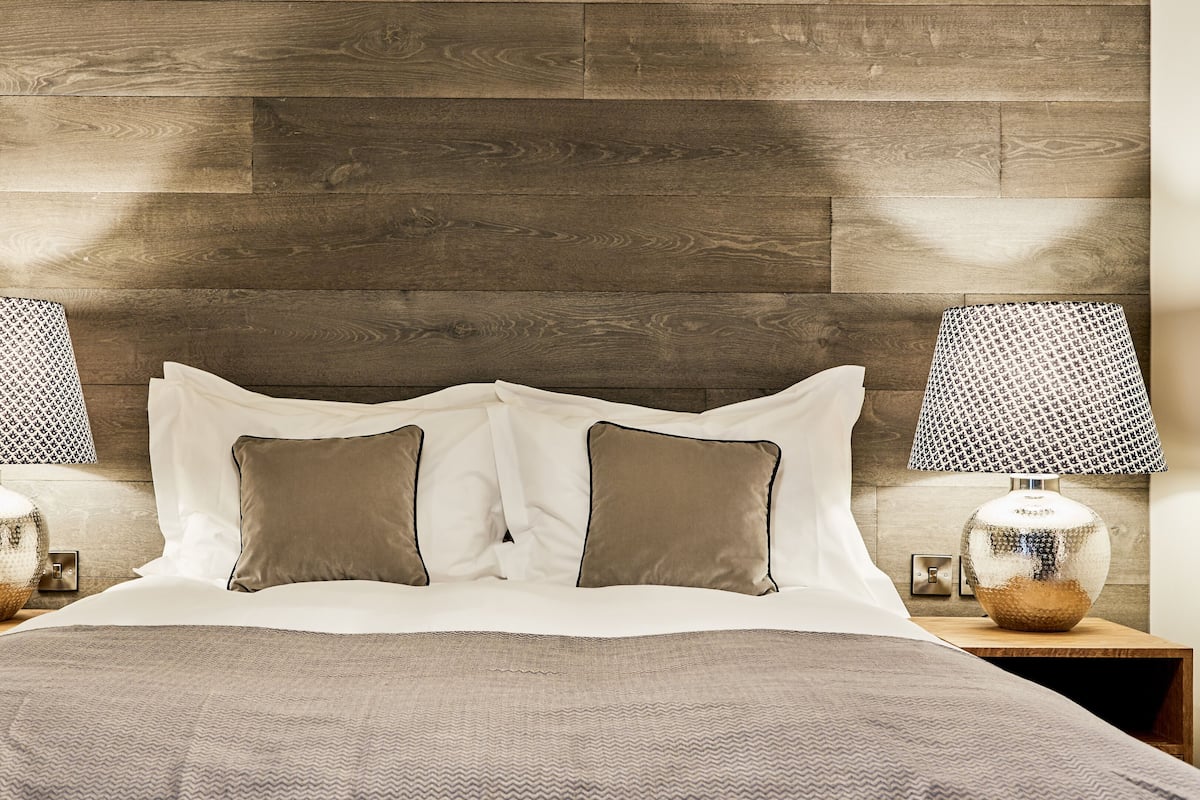 A bedroom with a wooden headboard, two bedside lamps, a telephone, and a patterned bedspread.