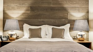 A bedroom with a wooden headboard, two bedside lamps, a telephone, and a patterned bedspread. - The Wellington Arms (Hook)