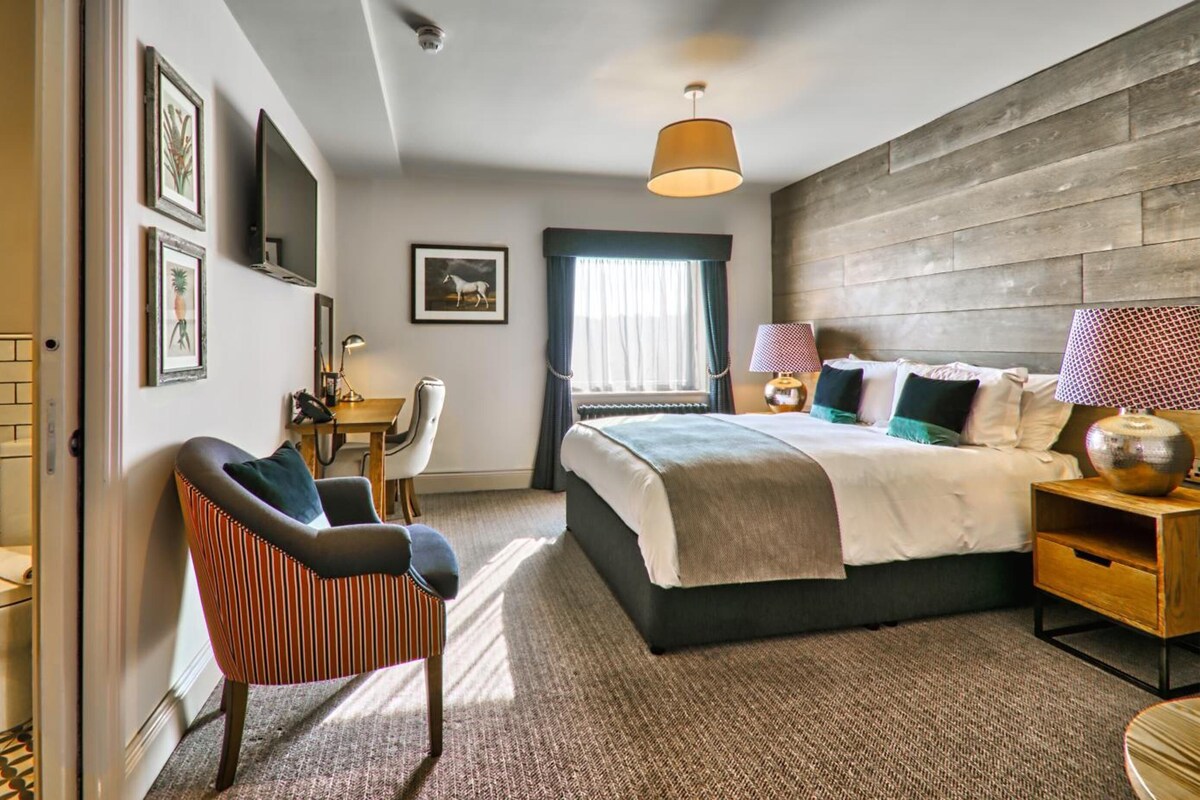 Une chambre à coucher comprenant un lit, une chaise, un bureau, une fenêtre avec des rideaux et un téléviseur fixé au mur.