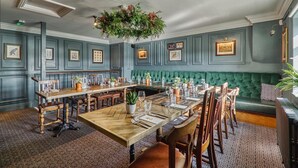 A dining area with a long wooden table, green upholstered bench, and framed pictures on the walls. - The Wellington Arms (Hook)