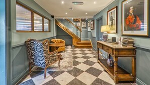 A hallway with a checkered floor, zebra-patterned chair, wooden desk, and framed portraits on the walls. - The Wellington Arms (Hook)