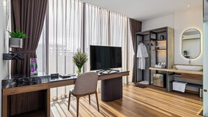 A modern hotel room with a large flat-screen TV, a wooden desk, a comfortable chair, a vanity with a mirror, and a wardrobe. - Hadiva Boutique Hotel (Da Nang)