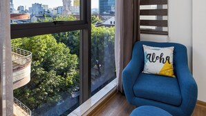 A room with a large window, a blue armchair, and a view of a cityscape. - Hadiva Boutique Hotel (Da Nang)