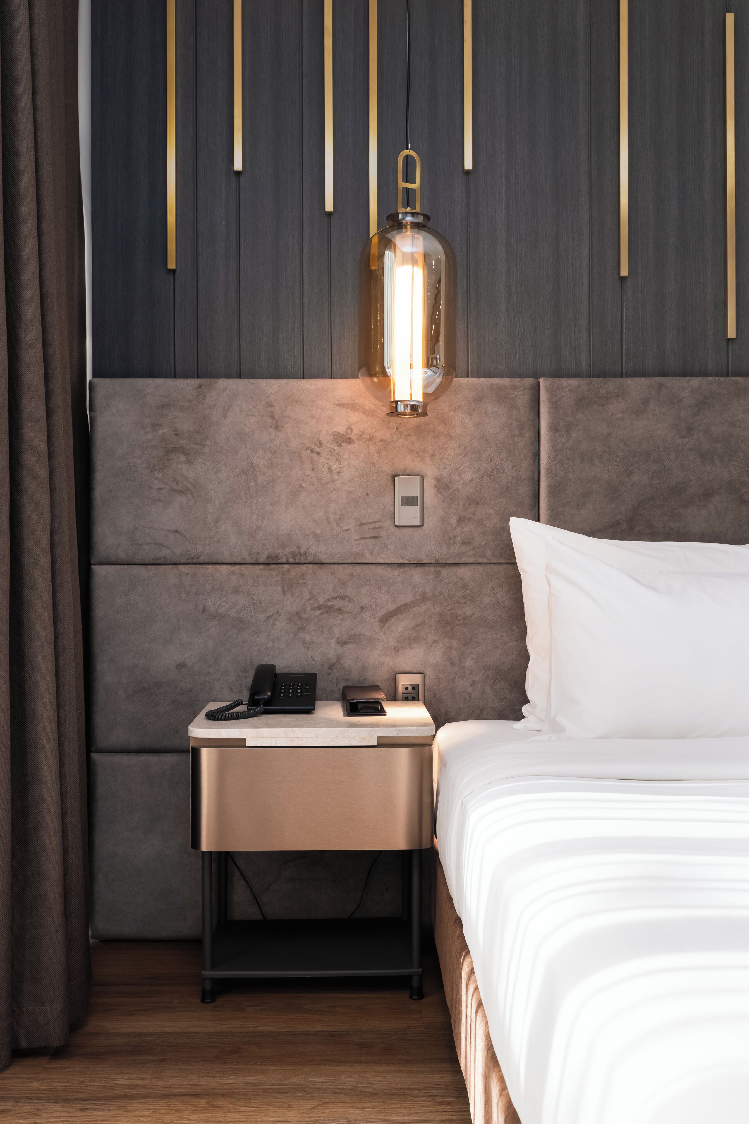 A modern hotel room with a large bed, a bedside table with a phone and a lamp, and a wall-mounted light fixture.