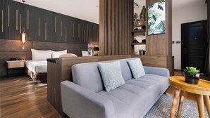 A modern bedroom with a grey sofa, a wooden headboard, and a small wooden table with a plant. - Hadiva Boutique Hotel (Da Nang)