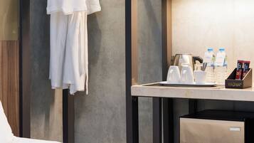 A hotel room with a bed, a robe rack with white robes, a small table with a coffee maker, cups, and a box of tissues.