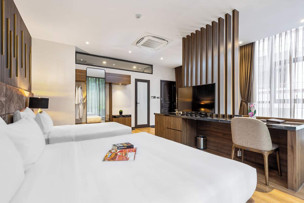 A hotel room with two beds, a kitchenette, a TV, and a large window with curtains.