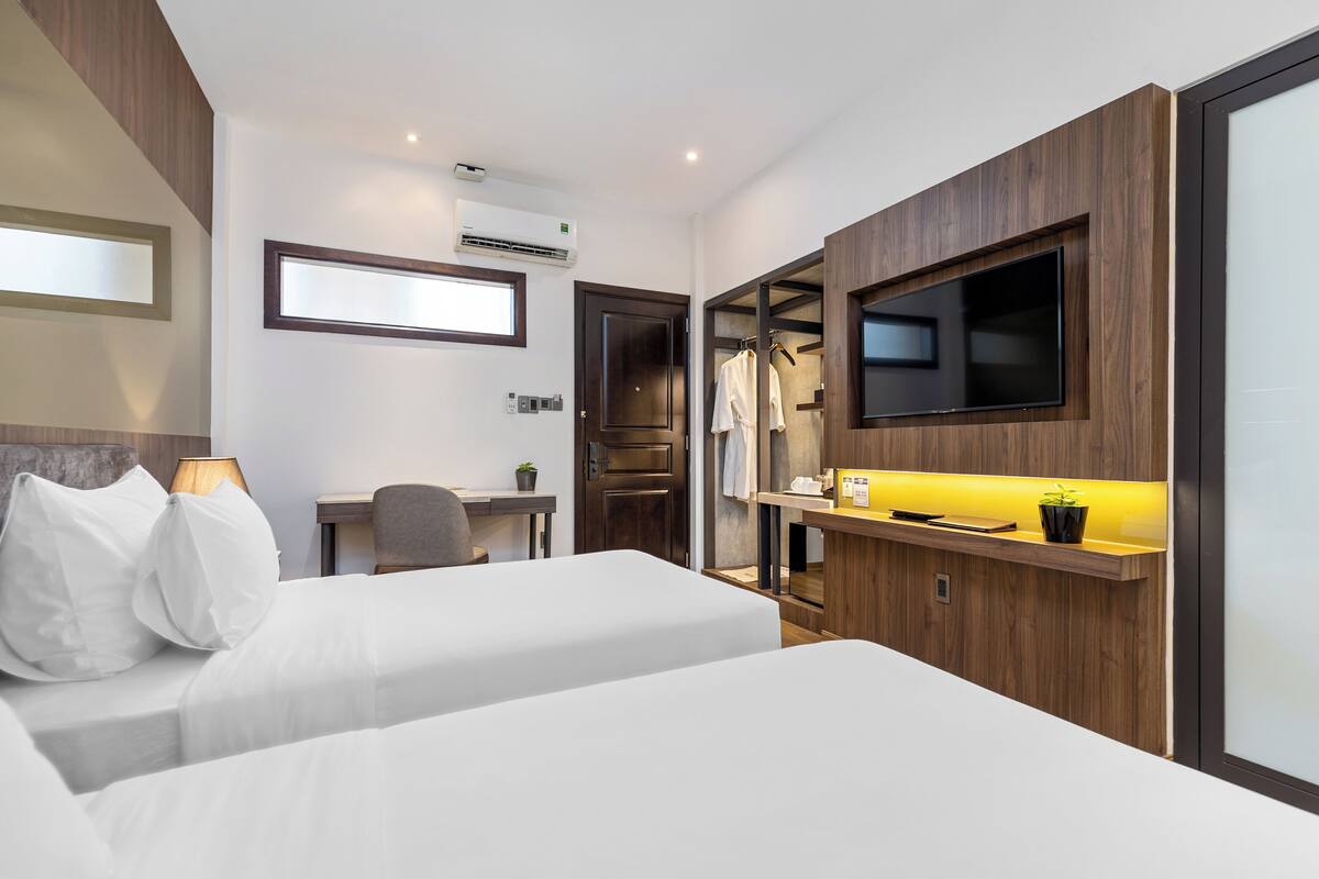 A hotel room with two beds, a desk, a chair, a TV, and a wardrobe.
