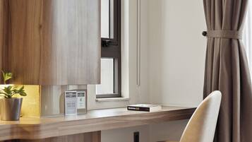 A hotel room with a wooden desk, a chair, a potted plant, and a window with curtains.