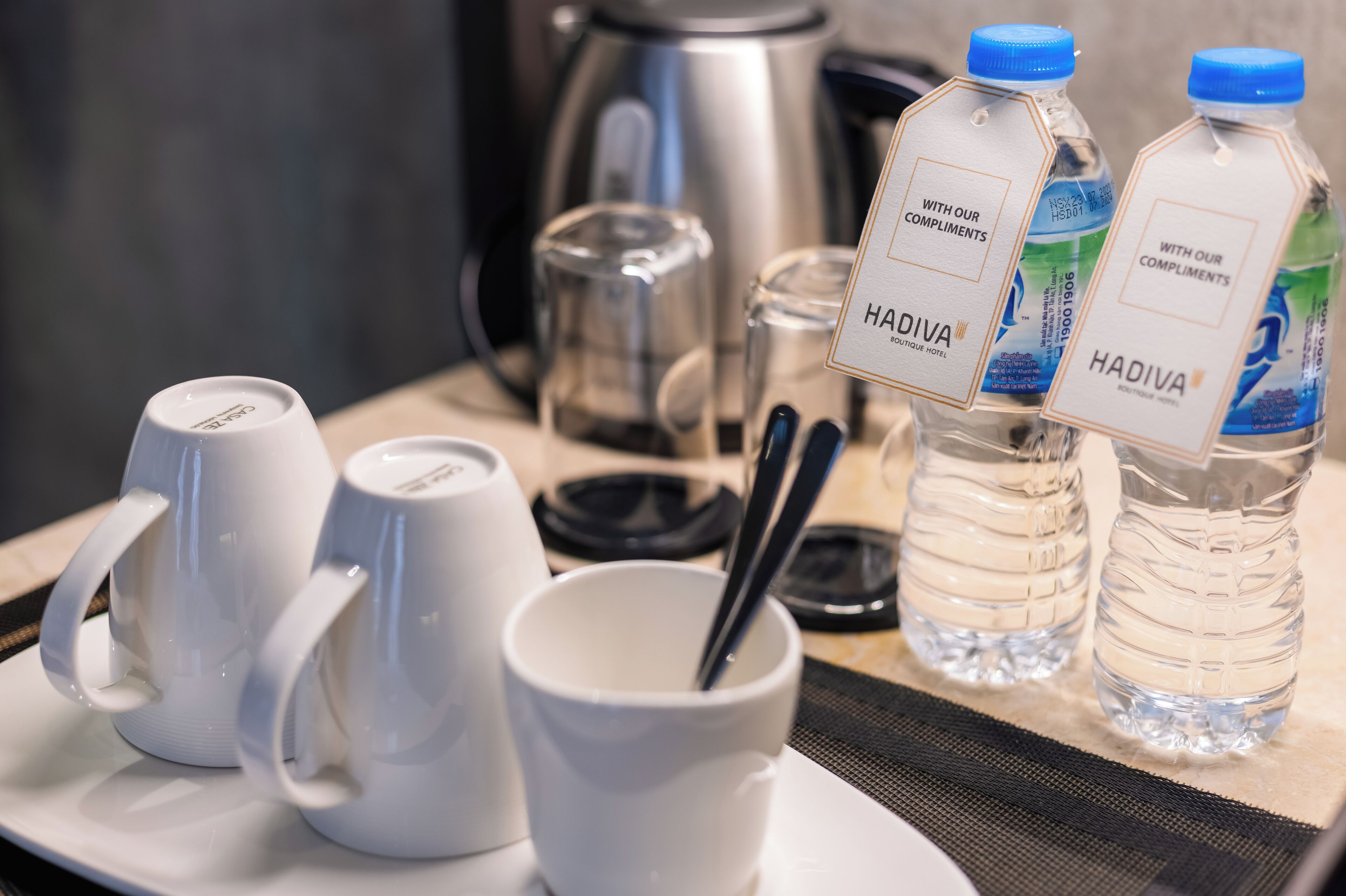 Un desayuno con tazas blancas, un vaso, una cuchara y dos botellas de agua con la etiqueta "HADIVA".