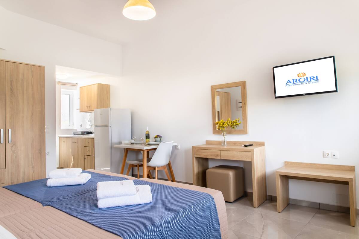 A hotel room with a bed, a desk, a chair, a small table, and a TV mounted on the wall.