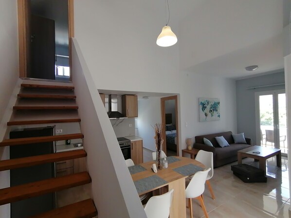 A modern living space with a wooden staircase, a dining area with a wooden table and chairs, a kitchen with wooden cabinets, a sofa, and a coffee table. - Argiri Apartments & Suites (Apokoronas)