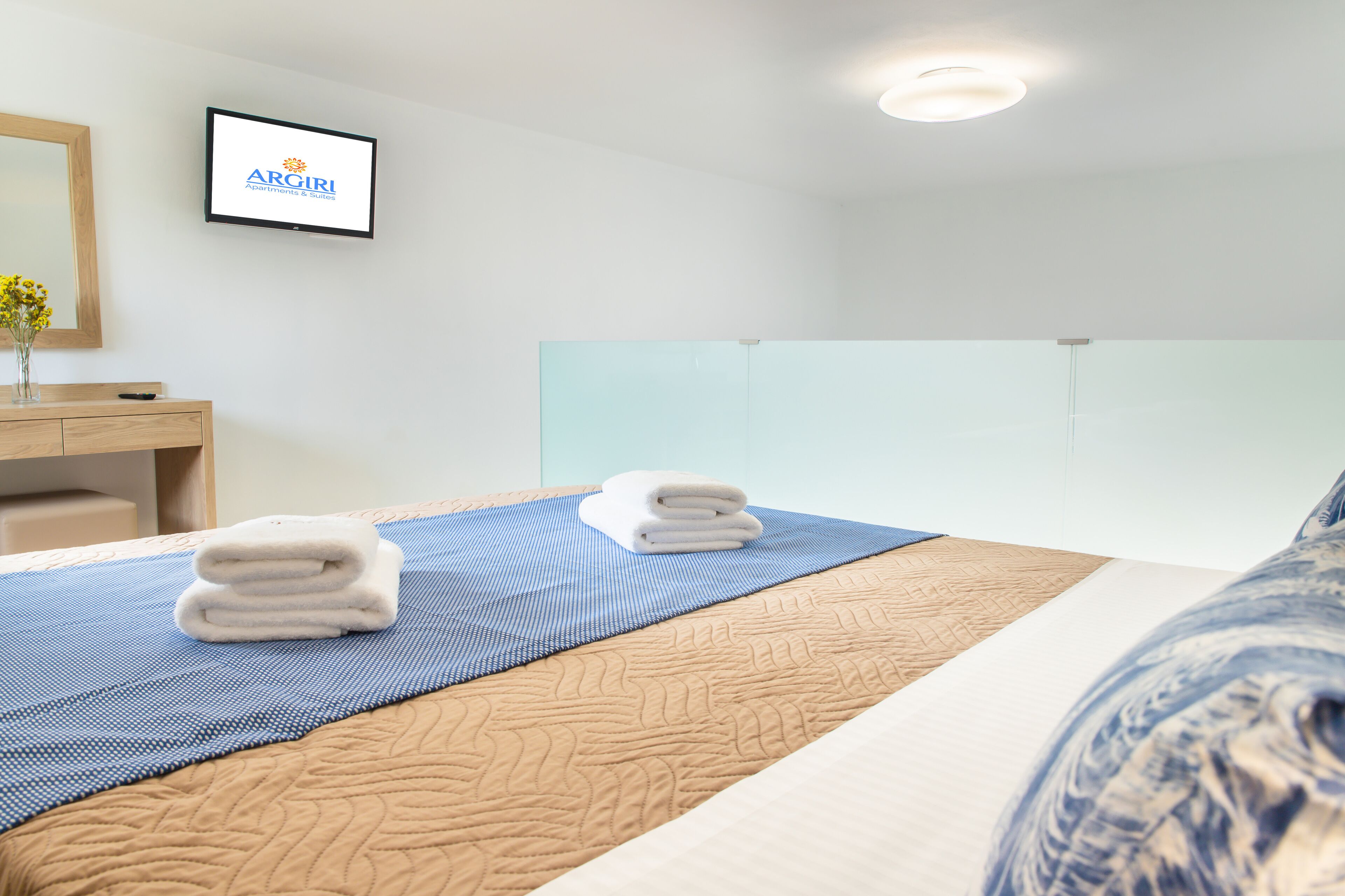 A hotel room with a bed, a blue and beige bedspread, a blue and beige pillow, a white towel, a wooden nightstand, a mirror, and a framed sign on the wall.