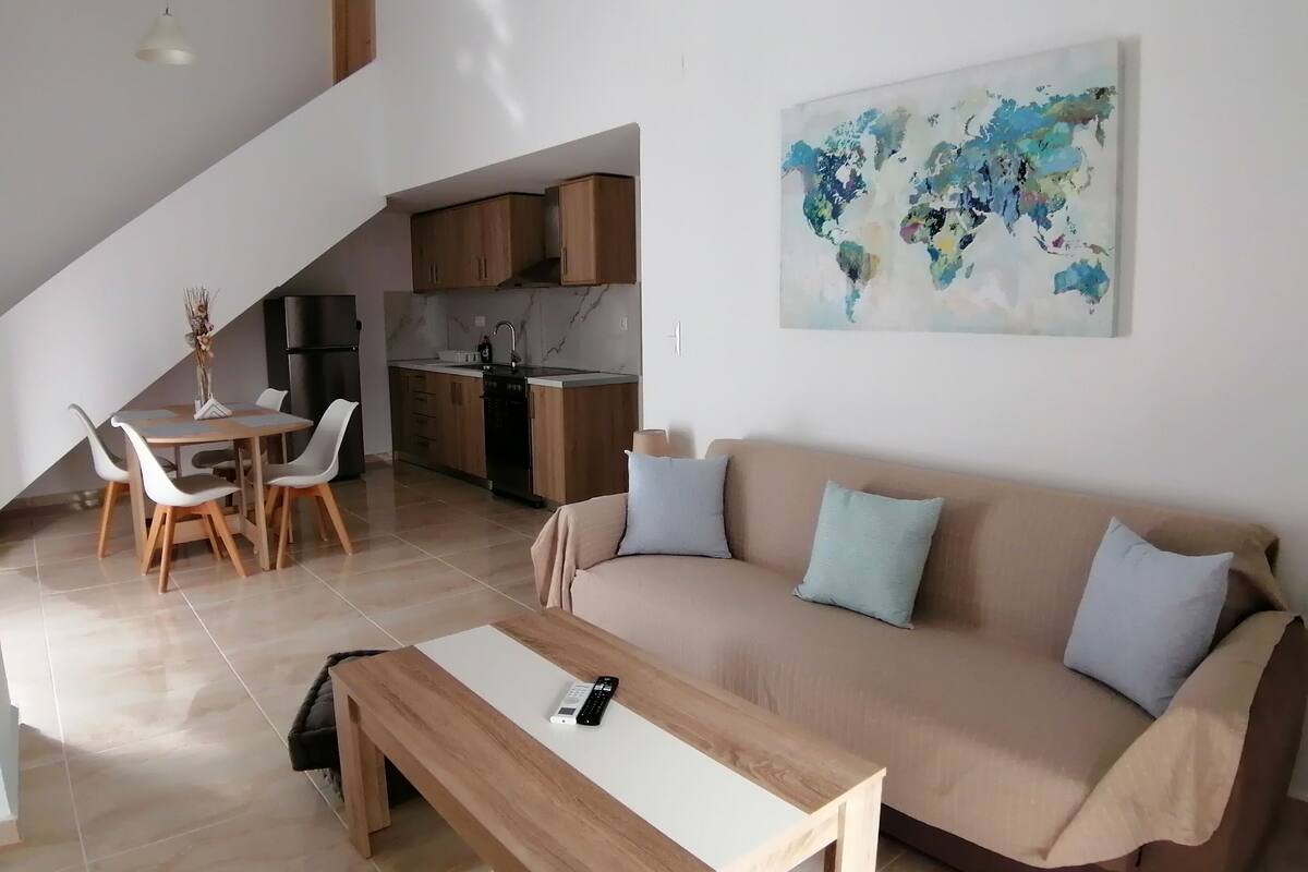 A modern living space with a dining area, kitchen, and a large sofa with cushions.