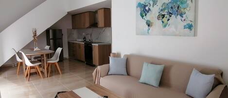 A modern living space with a dining area, kitchen, and a large sofa with cushions.
