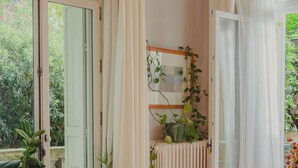 Un coin repas avec une table en bois et des chaises en osier, entouré de plantes en pot et offrant une vue sur la verdure à l’extérieur.