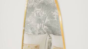 A mirror with a tree and flower pattern, a white sofa, and two pillows with a leaf pattern.