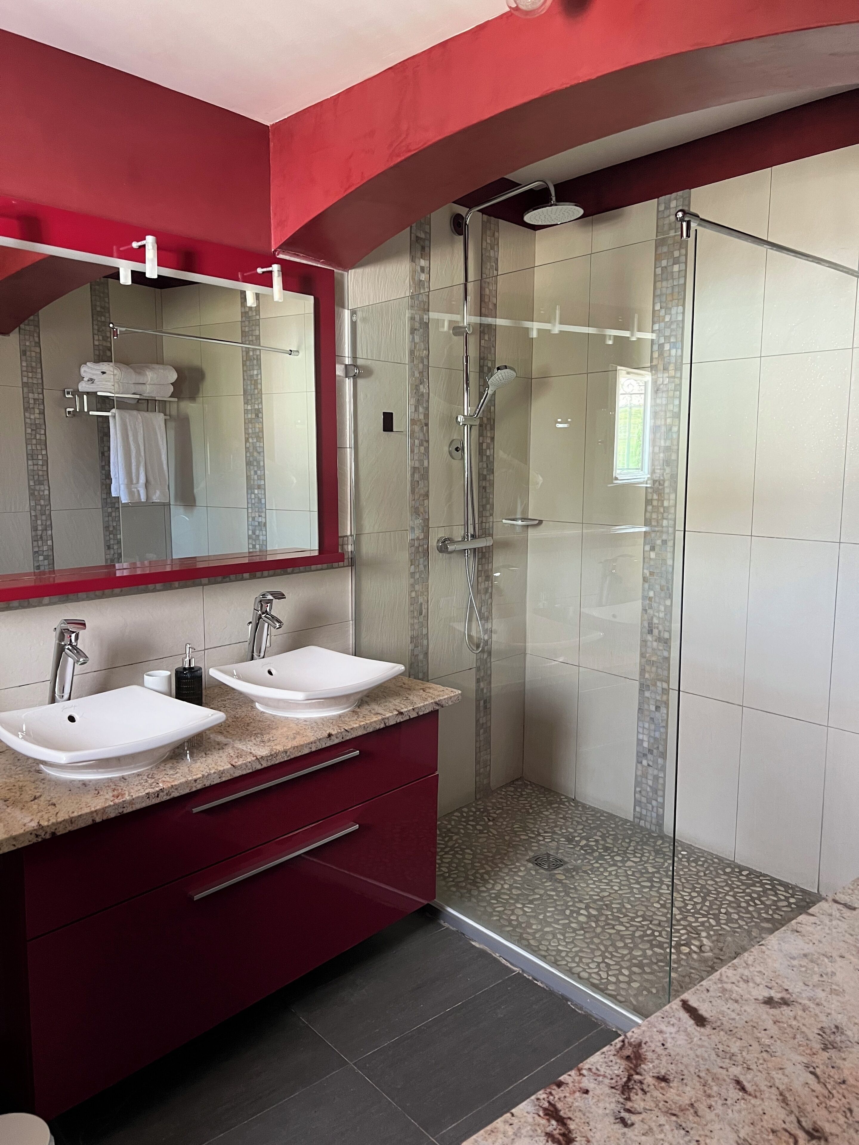 A modern bathroom with two sinks, a glass shower enclosure, and a red vanity.