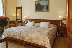 Una habitación de hotel con una cama grande, dos mesitas de noche, un tocador, un espejo y un cuadro en la pared.