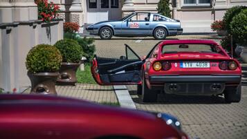 Un coche deportivo rojo aparcado frente a un edificio, con una furgoneta de reparto azul al fondo.