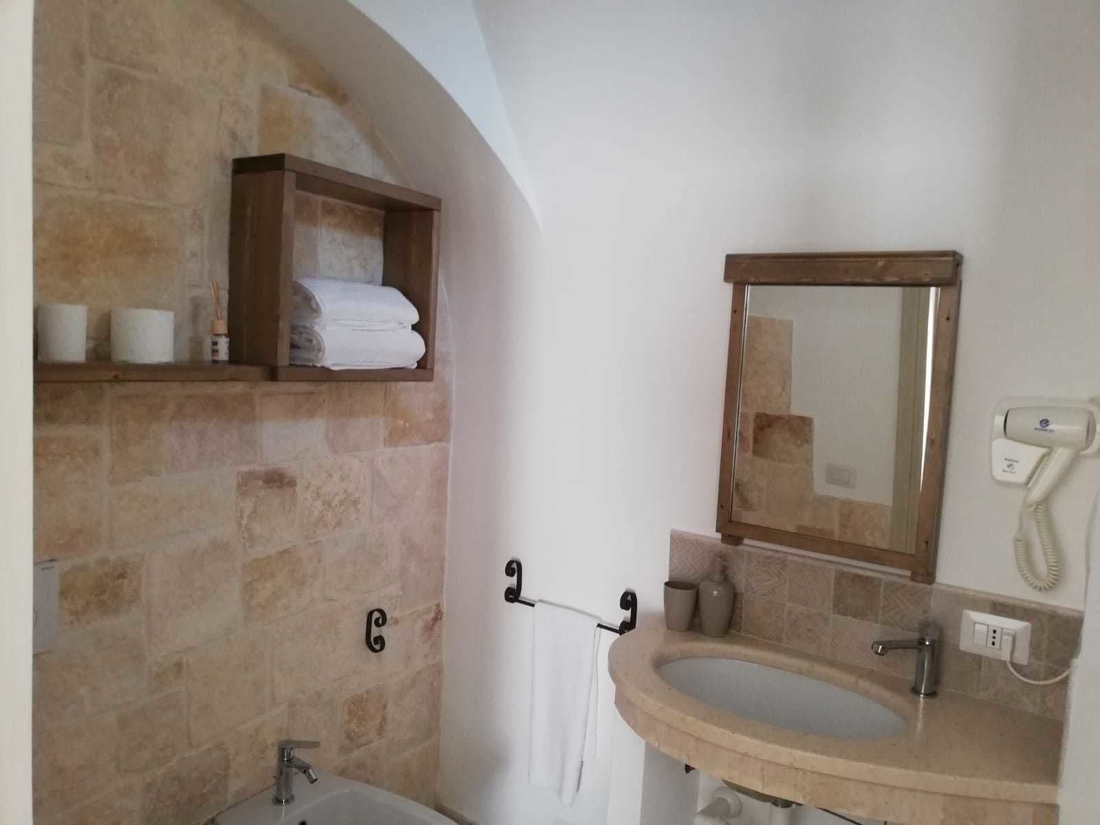 Une salle de bain avec un mur en pierre, une étagère en bois avec des serviettes, un miroir, un lavabo, un sèche-cheveux et un porte-serviettes.
