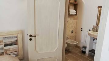 A bedroom with a bed, a door leading to a bathroom with a sink, toilet, and shower.