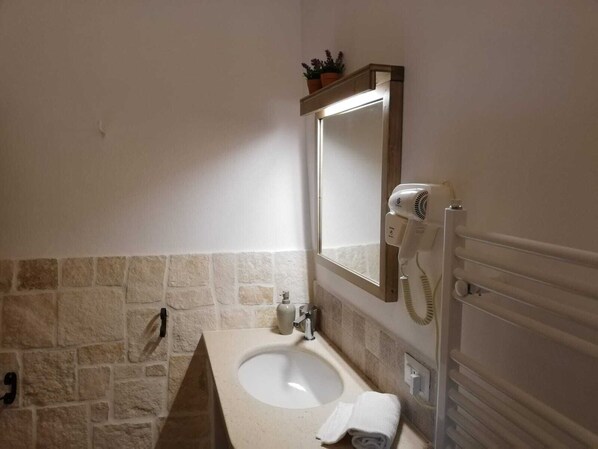 A bathroom with a stone wall, a white sink, a mirror, a hairdryer, and a towel.