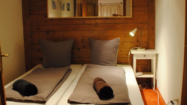 A room with two beds, wooden beams, a mirror, a nightstand, and a lamp. - Haus Zentral (Sankt Anton am Arlberg)