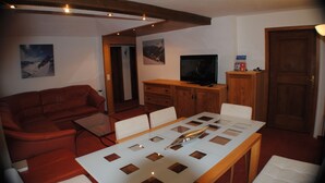 A living room with a red sofa, a dining table with a decorative centerpiece, wooden cabinets, and a television. - Haus Zentral (Sankt Anton am Arlberg)