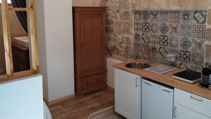 Une cuisine compacte avec un pare-feu en pierre, des armoires en bois et un lave-vaisselle encastré.