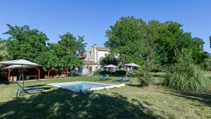 Une piscine avec des chaises longues, un gazebo et une maison avec un toit en tuiles.
