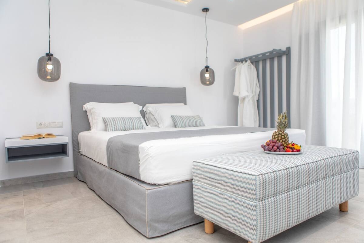 A modern bedroom with a large bed, bedside tables, a patterned ottoman, and a fruit plate on the nightstand.
