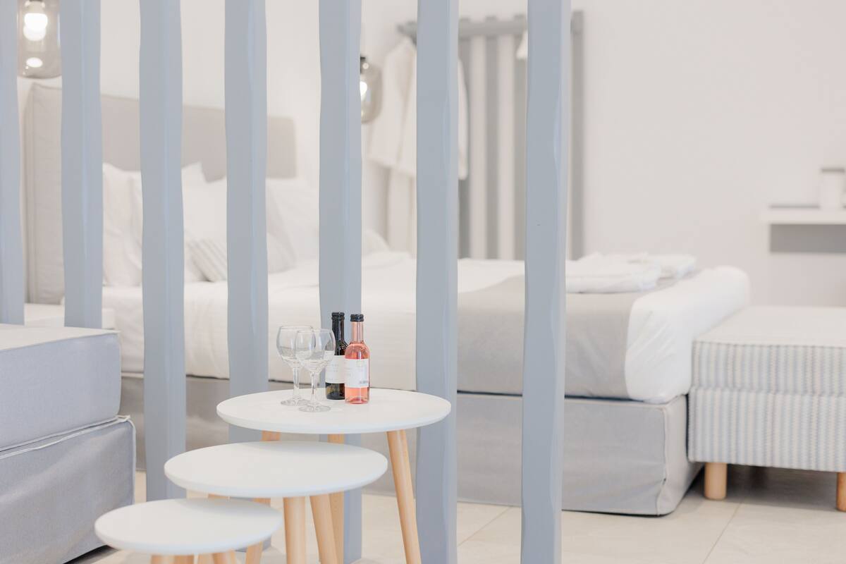 A modern hotel room with a bed, a small round table with wine bottles and glasses, and a grey sofa.