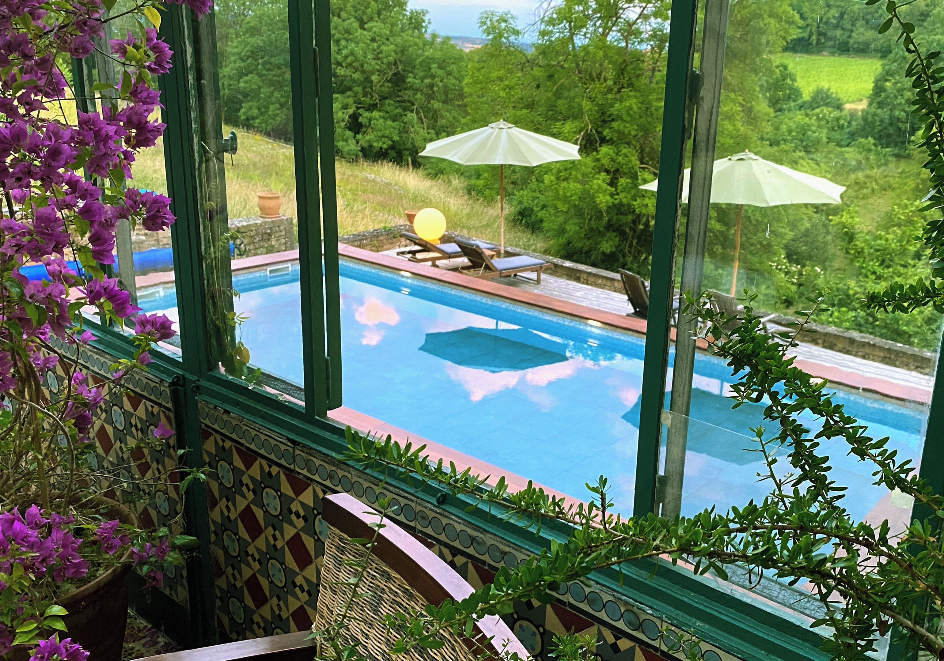 Une piscine agrémentée de deux parasols, entourée d’une végétation luxuriante et offrant une vue sur la campagne.
