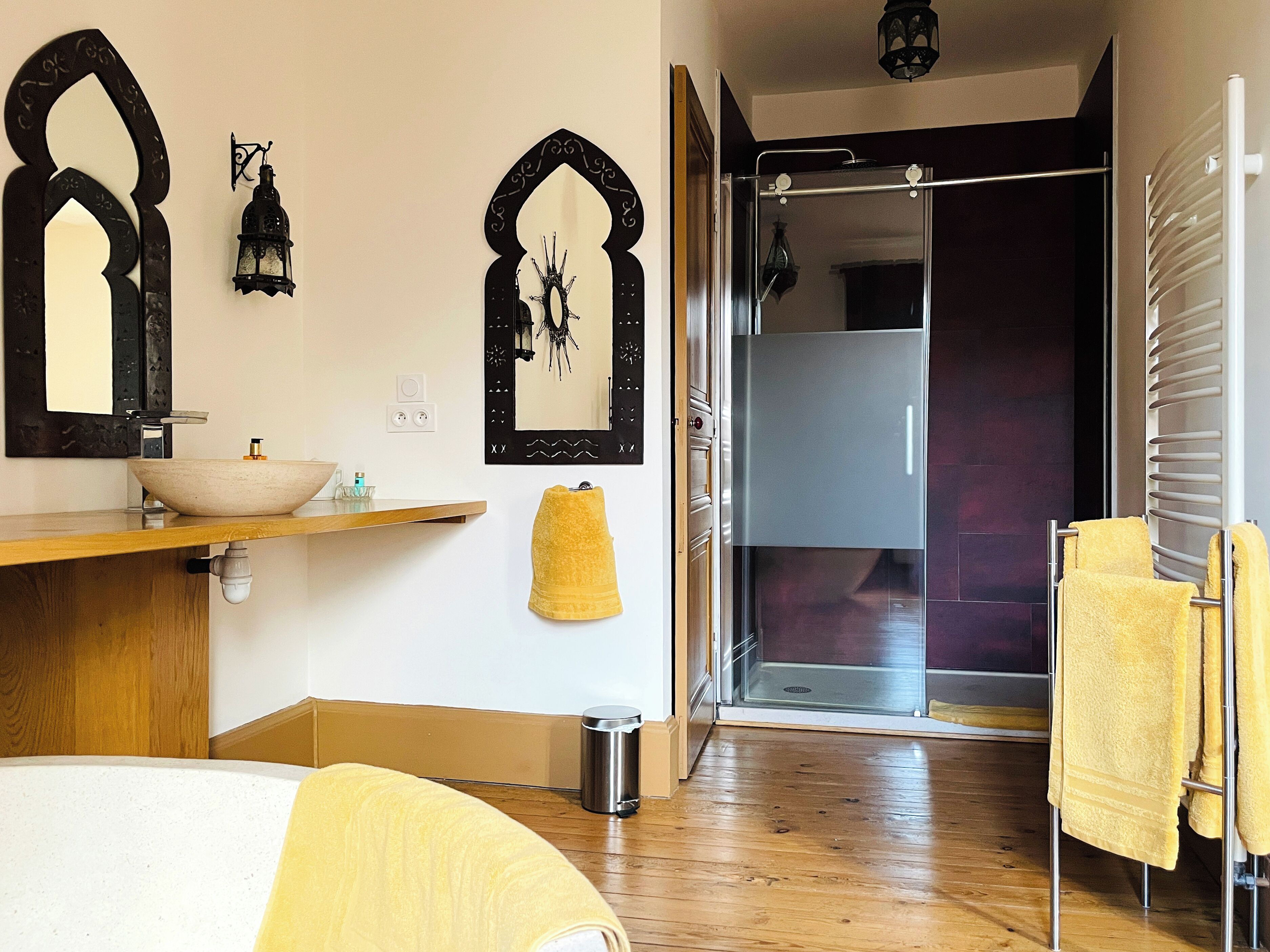 A modern bathroom with a wooden vanity, a large mirror, a vessel sink, a towel rack, and a glass shower enclosure.