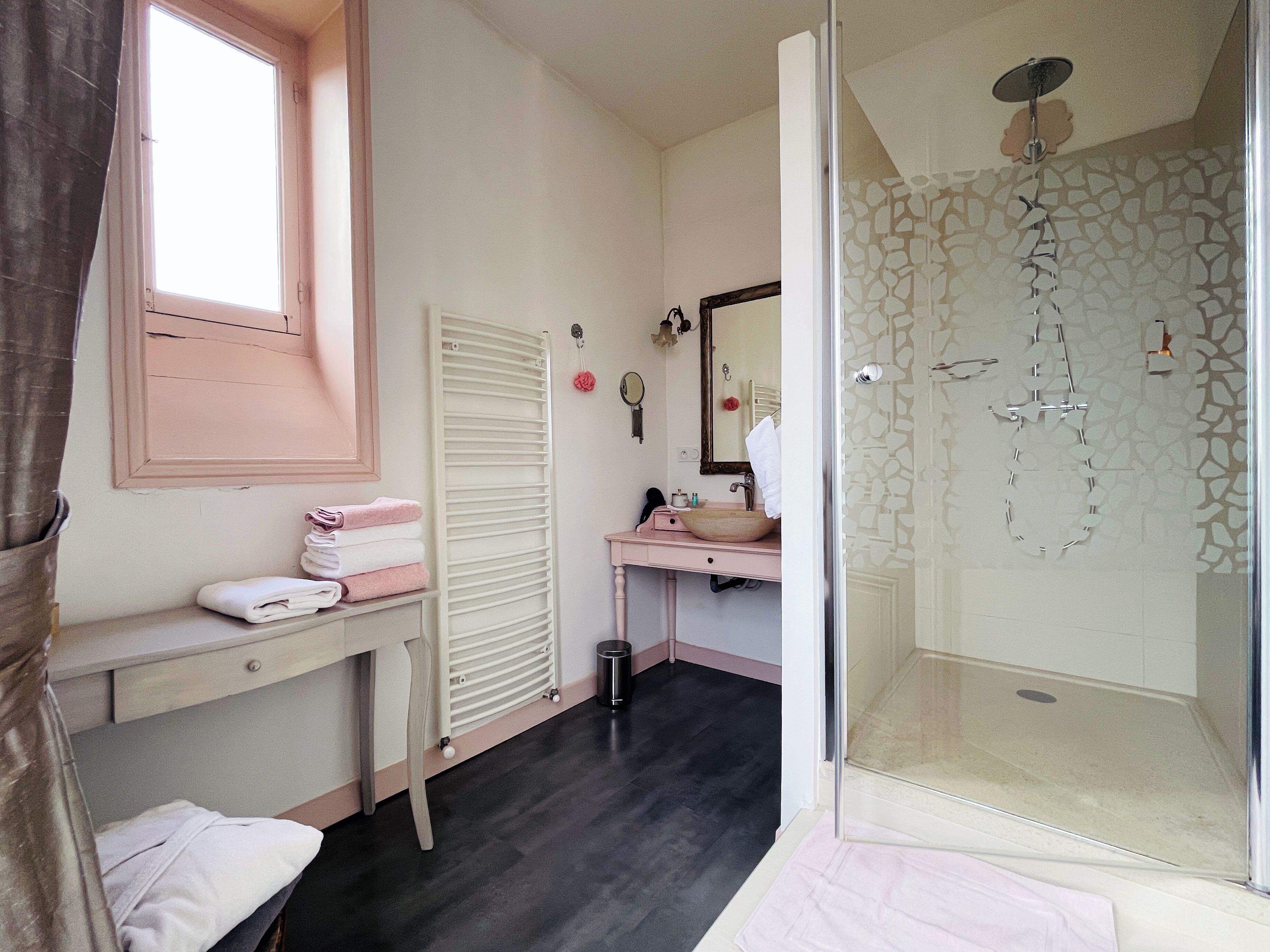 Ein Badezimmer mit Glasdusche, Waschbecken mit Spiegel, Handtuchhalter und Heizkörper.