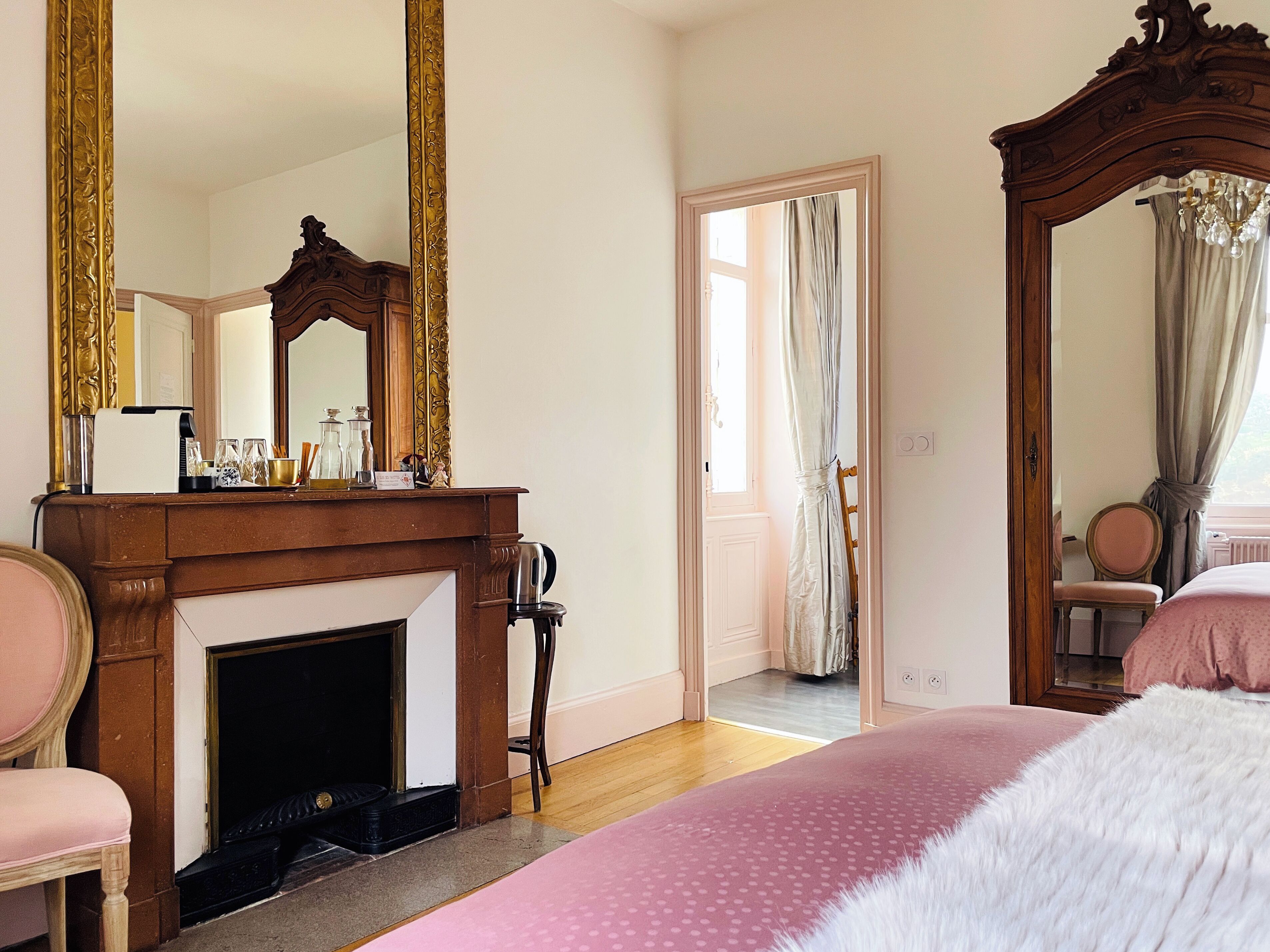 Un dormitorio con chimenea, un espejo grande y una cama con colcha rosa.