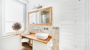 A modern bathroom with a large mirror, a wooden vanity, a white sink, and a decorative plant. - Ferienwohnungen Casa Bella Cosa (Braunlage)