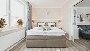 A bedroom with a large bed, a headboard with a deer head, and a window with curtains. - Ferienwohnungen Casa Bella Cosa (Braunlage)