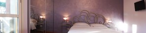 Une chambre à coucher avec un lit, deux tables de chevet avec des lampes, un miroir et une fenêtre.