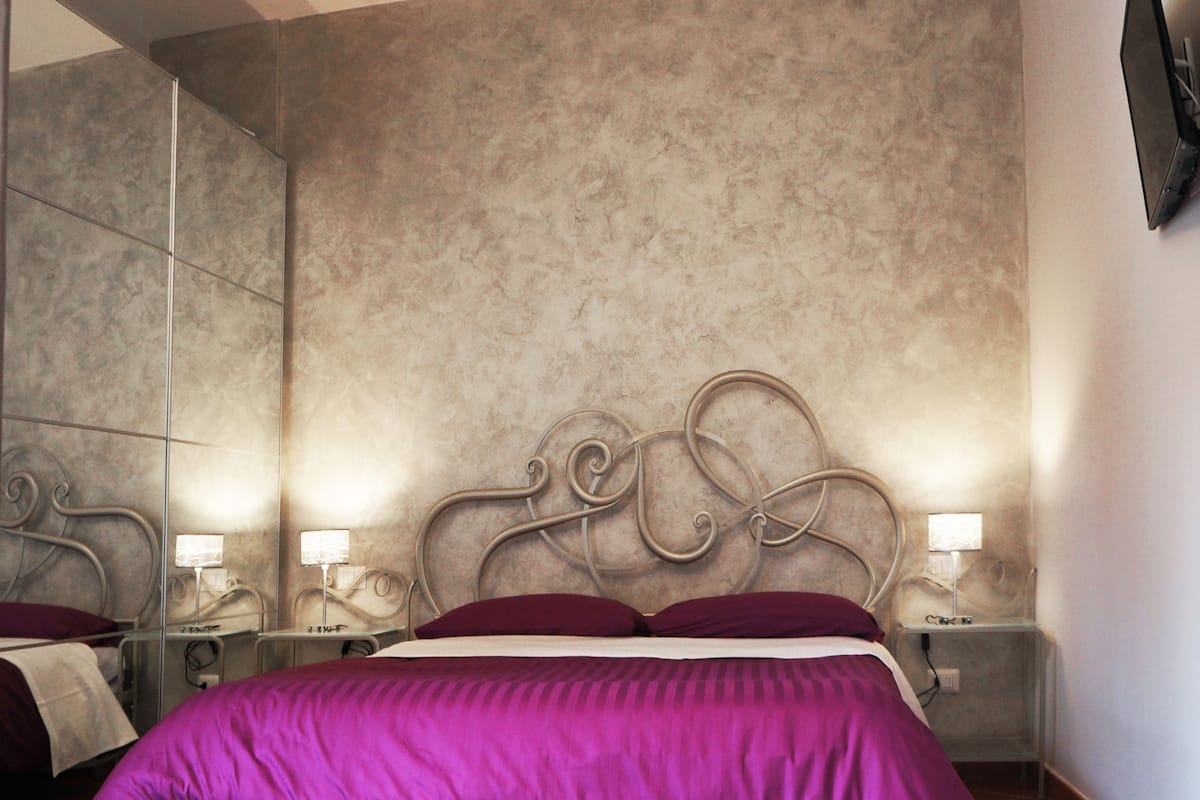 A bedroom with a large bed, two bedside tables with lamps, a mirror, and a textured wall.