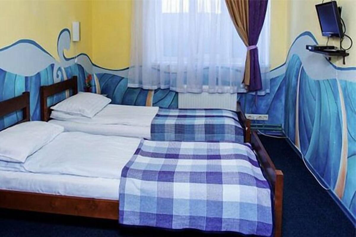 A room with two beds, a wooden nightstand, a desk, and a wall with a wavy design.