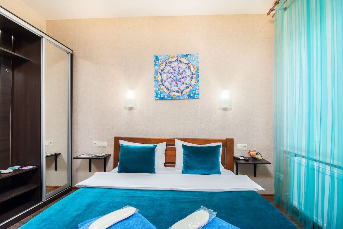 A hotel room with a bed, a wardrobe, a painting on the wall, and a window with curtains.