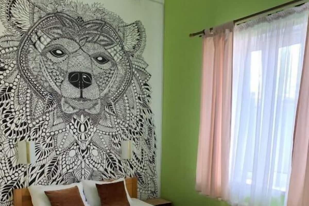 A bedroom with a large wall mural, a bed with brown bedding, and a window with sheer curtains.